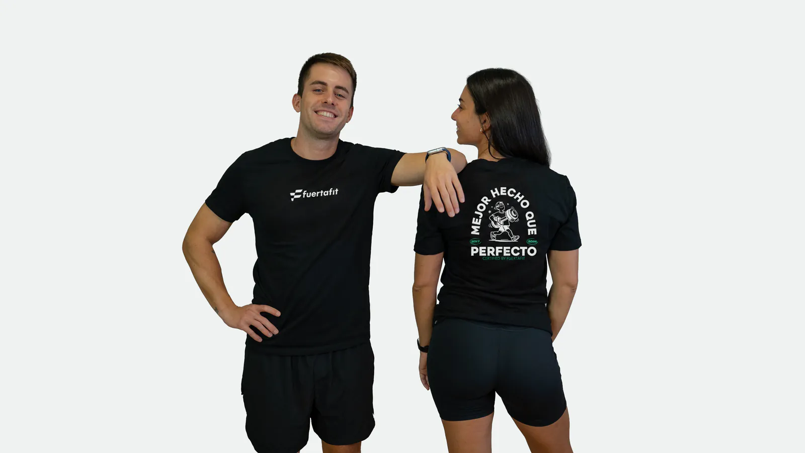 Dos entrenadores de Fuertafit con la camiseta negra Mejor hecho que perfecto ilustrada: él de frente y ella de espaldas